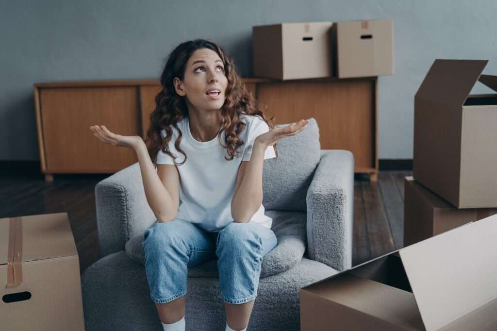 Puzzled divorced girl exclaims shrugging sitting with boxes for relocation. Divorce, hard moving day